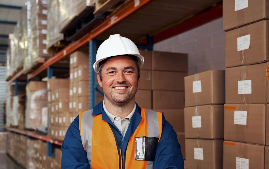 Smiling battery technician wearing a safety vest and hard hat in a warehouse