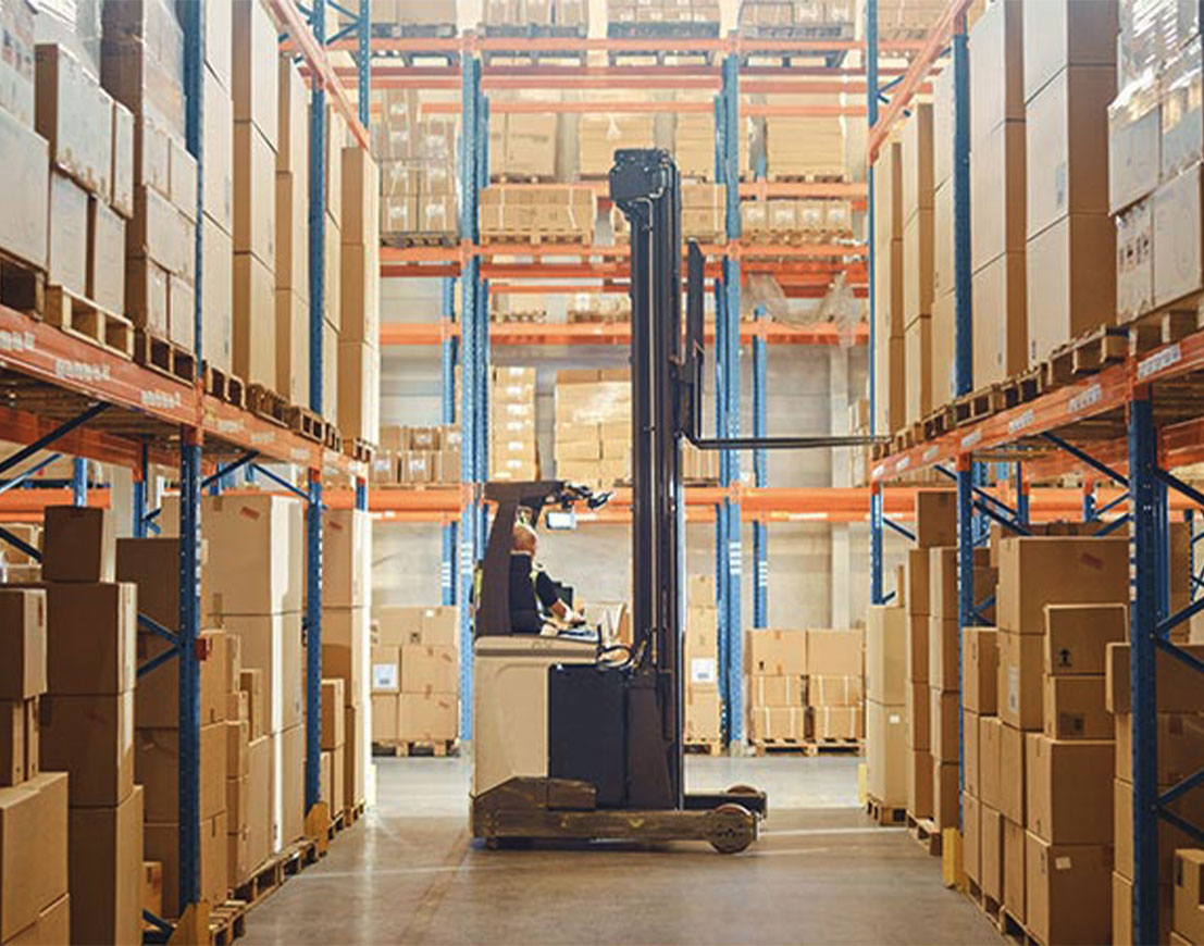 Retail warehouse full of shelves with goods: Electric Forklift Truck operator lifting pallet with cardboard box on a shelf. Working in logistics storehouse product logistics and delivery center.